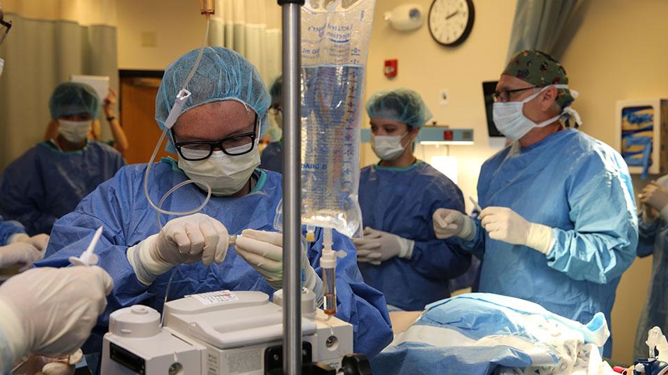 A person connects an IV tube to a monitor in an operating room